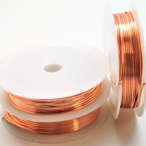 Peut inclure: Trois bobines de fil de cuivre. Deux bobines sont empilées et la troisième est droite. Le fil est enroulé serré sur des bobines en plastique blanc. Le fil de cuivre a un aspect brillant et métallique, idéal pour la bijouterie ou l'artisanat.