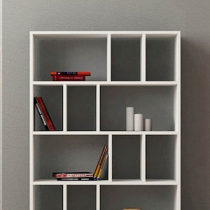 May include: White bookshelf with 12 compartments. The shelves are empty except for a few books and decorative items. The books include "Anatomy for Artists" and "Understanding the Nude".