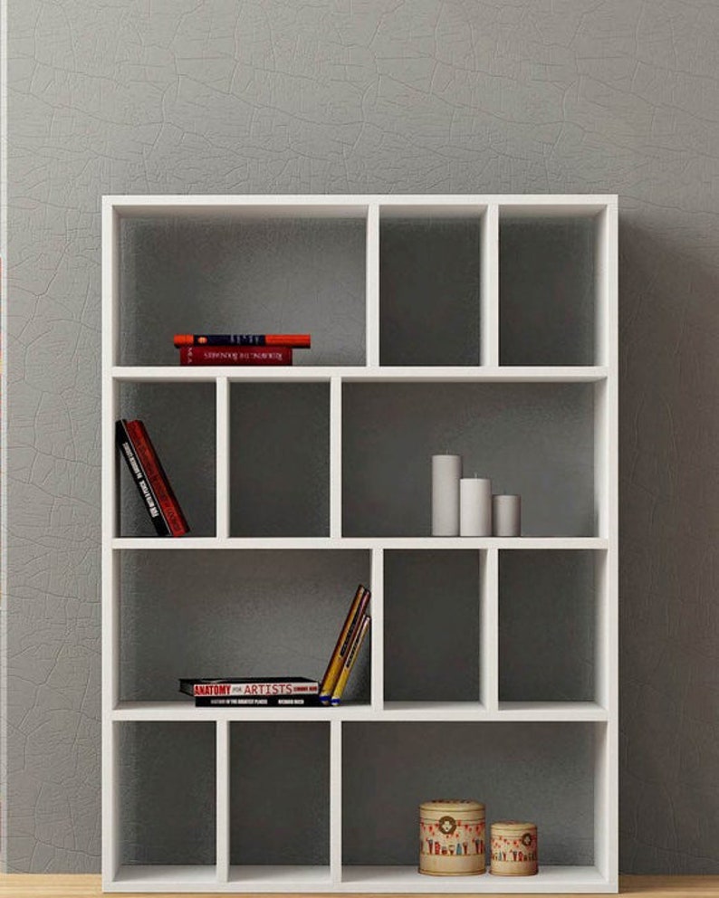 May include: White bookshelf with 12 compartments. The shelves are empty except for a few books and decorative items. The books include "Anatomy for Artists" and "Understanding the Nude".