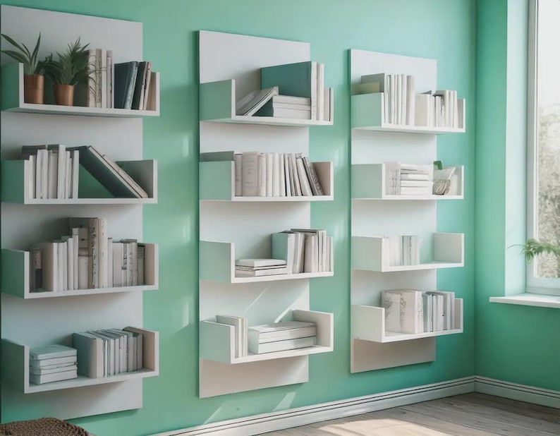 Puede incluir: Estanter&iacute;as blancas montadas en la pared con m&uacute;ltiples estantes, cada uno con una colecci&oacute;n de libros. Algunos estantes tambi&eacute;n exhiben peque&ntilde;as plantas en macetas. Las estanter&iacute;as est&aacute;n contra una pared verde claro, creando un aspecto moderno y organizado.
