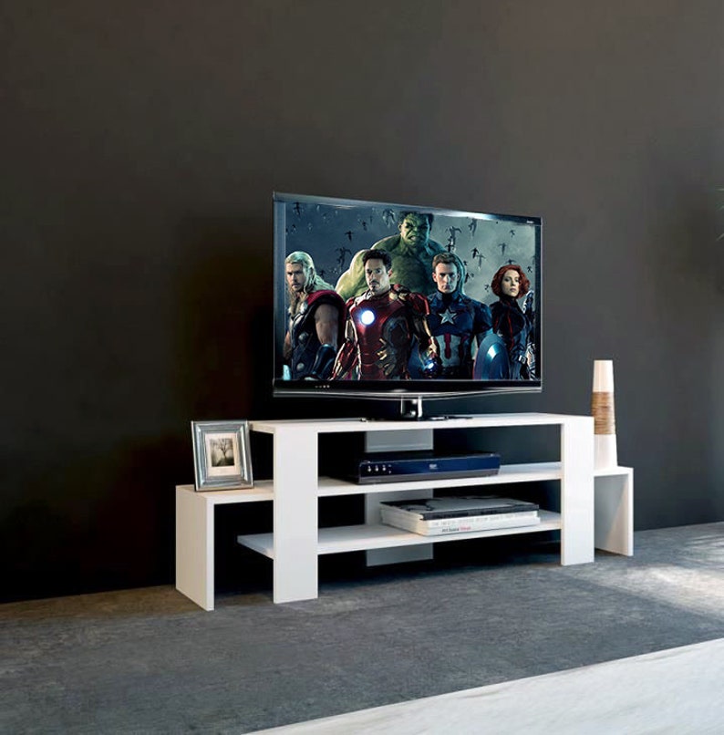 May include: White entertainment center with three shelves, a black glass top, and a flat screen TV playing a movie. The TV is on a white stand with a black glass top. The entertainment center is in a room with a gray wall.