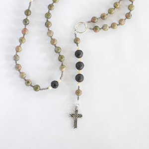 Puede incluir: Un rosario de piedra verde, marrón y blanca con cuentas de lava negra y una cruz de plata.