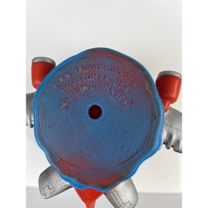 Puede incluir: Una figura de juguete vintage con una base azul y detalles rojos. El texto en la base dice "B.K.B. 'KOOL' BUDDIES HOUSTON TX. USA MADE IN CHINA 1993". La figura tiene brazos plateados y formas cil&iacute;ndricas rojas.