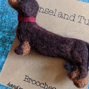 May include: A brown and tan felt dachshund brooch with a red felt collar. The brooch is handmade in Shropshire and is part of a collection of brooches.