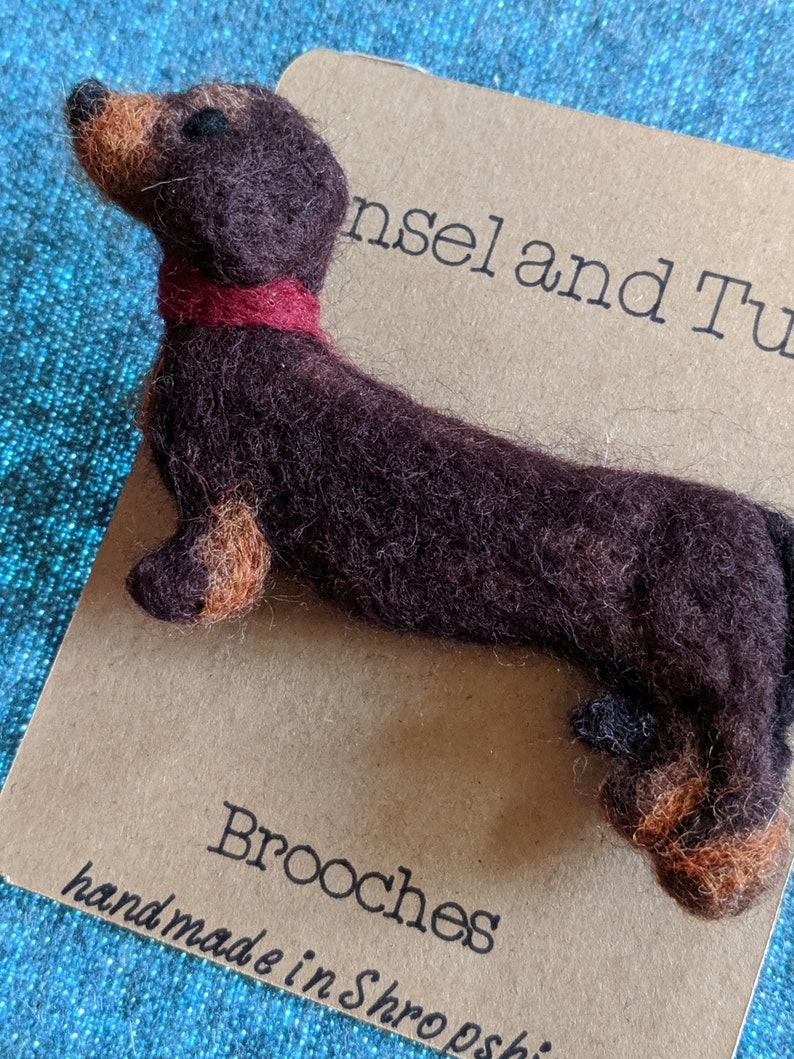 May include: A brown and tan felt dachshund brooch with a red felt collar. The brooch is handmade in Shropshire and is part of a collection of brooches.