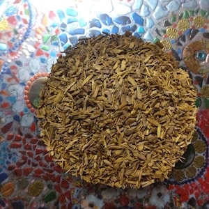 May include: A close-up of a bowl filled with dried, brown, shredded bark. The bark is in a pile in the center of the bowl. The bowl is on a colorful, mosaic surface.