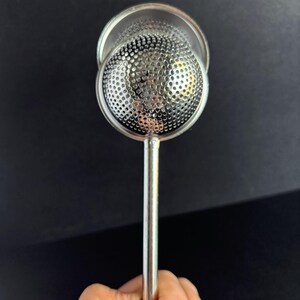 May include: A silver-colored metal tea infuser featuring a spherical, perforated mesh head attached to a straight, slender handle. The circular mesh component is designed to hold loose tea leaves, with a polished metallic finish throughout.