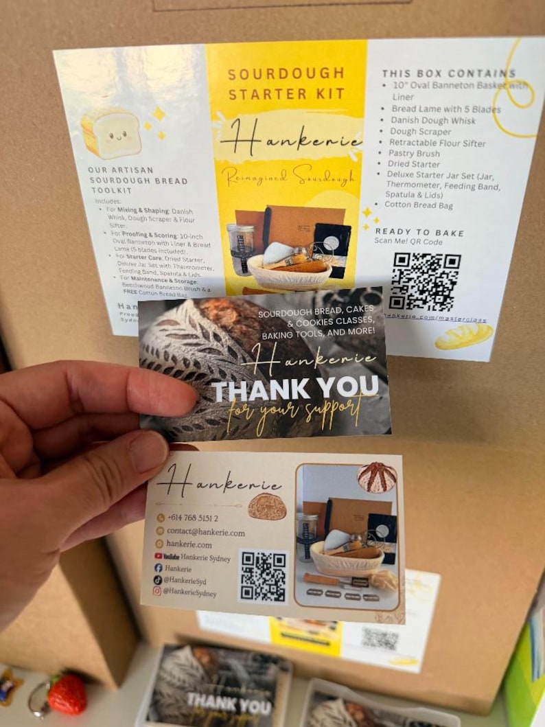 May include: A Sourdough Starter Kit box with an informational insert listing contents like a 10-inch oval banneton, bread lame, dough whisk, and flour sifter. Two thank you cards from Hankerie are held in front, displaying contact details and QR codes.