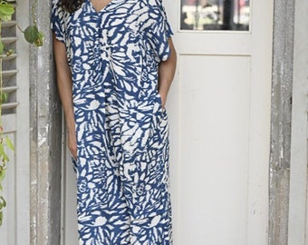Puede incluir: Una mujer con un vestido midi de manga corta con estampado azul y blanco. Está de pie frente a una puerta blanca con una ventana.