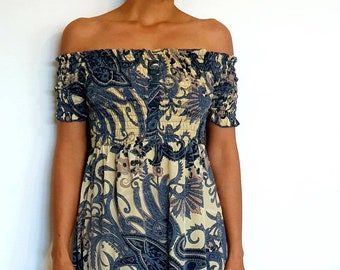 May include: A blue and beige off-the-shoulder dress with a paisley print and a high-low hemline. The dress has a ruffled hem and a fitted bodice.