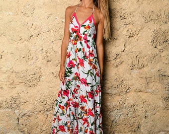May include: A white maxi dress with a floral print featuring red, pink, and yellow flowers. The dress has a halter neckline and a tiered skirt.