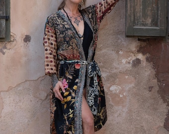 May include: A long, patterned robe with a floral and paisley design. The robe features a mix of colors, including black, beige, red, and yellow. It is tied at the waist with a matching belt. The sleeves have a patterned design.