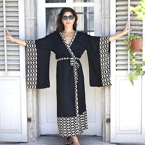 Könnte beinhalten: Schwarzer Kimono-Stil-Robe mit weiten Ärmeln und Wickeldesign. Die Robe hat ein geometrisches Muster in Weiß und Beige an Ärmeln, Saum und Gürtel. Die Robe ist bodenlang und aus leichtem Stoff gefertigt.