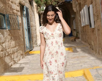 May include: A woman in a white floral maxi dress walks down a stone pathway in a city. The dress has a V-neckline and short sleeves.