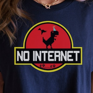 May include: A navy blue t-shirt featuring a pixelated dinosaur wearing a party hat. The dinosaur is inside a red circle with a yellow border. The text "NO INTERNET" is below the dinosaur.