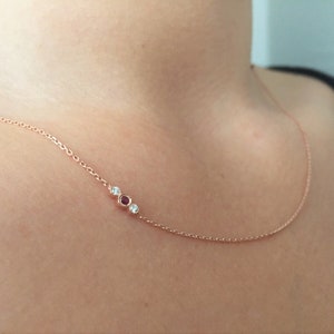 Puede incluir: Un delicado collar de cadena de oro con tres pequeñas piedras preciosas: dos diamantes transparentes y un rubí rojo.