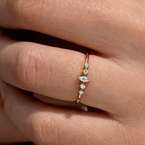 May include: A delicate gold ring with a marquise-shaped diamond in the center and smaller round diamonds on either side. The ring is set on a thin band.