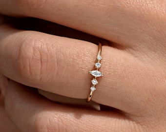 May include: A delicate gold ring with a marquise-shaped diamond in the center and smaller round diamonds on either side. The ring is set on a thin band.
