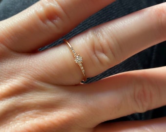 May include: A delicate gold ring with a small diamond in the center and smaller diamonds set along the band.