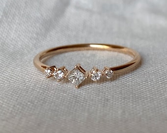 May include: A delicate gold ring featuring a row of small diamonds, including a larger square-shaped diamond in the centre.