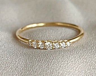 May include: A delicate gold band ring with a row of small, clear diamonds set in a straight line.