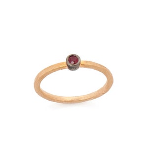 May include: A simple gold band ring with a single red gemstone set in a silver bezel.