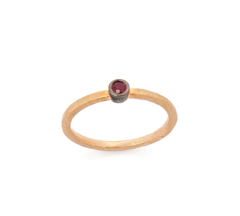 May include: A simple gold band ring with a single red gemstone set in a silver bezel.