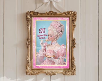 Può includere: Stampa incorniciata con una cornice dorata ornata, raffigurante una donna in abito rosa e acconciatura elaborata, che mangia una torta. L'opera d'arte include il testo "CAKE FIRST, REVOLUTION LATER." La stampa è appesa a una parete di legno bianca.