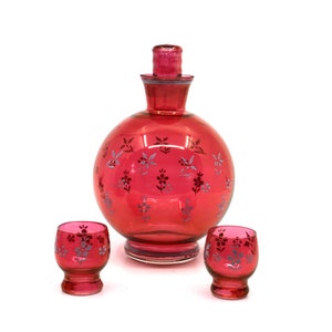 May include: A set of three red glass decanters with a floral pattern. The decanters are made of clear glass with a red tint and have a silver floral pattern.