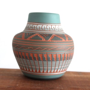 May include: A teal-colored ceramic vase with intricate geometric patterns in orange, gray, and white. The vase features a rounded body and a slightly flared neck, showcasing a blend of traditional and modern design elements. The vase is a decorative item.
