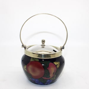 May include: A dark blue ceramic sugar bowl with a silver rim, lid, and handle. The bowl is decorated with a colorful fruit design featuring red apples and purple grapes. The handle is arched and attached to the bowl.