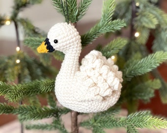 May include: A white crocheted swan ornament with black eyes and a yellow beak hanging on a small artificial Christmas tree.