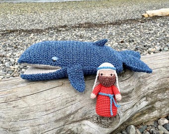 May include: A crocheted blue whale with a white mouth and a crocheted man with a red robe and a beard standing on a wooden log.