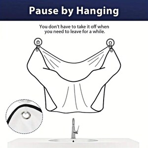 Op de afbeelding: Een witte stoffen kapperscape met twee haken om op te hangen. De cape is ontworpen om kleding te beschermen tegen haarsnippers tijdens het knippen. De tekst "Pause by Hanging" en "You don't have to take it off when you need to leave for a while." staat op de afbeelding.