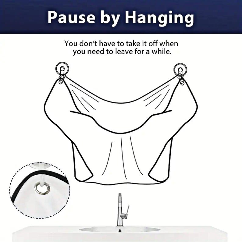 Op de afbeelding: Een witte stoffen kapperscape met twee haken om op te hangen. De cape is ontworpen om kleding te beschermen tegen haarsnippers tijdens het knippen. De tekst "Pause by Hanging" en "You don't have to take it off when you need to leave for a while." staat op de afbeelding.