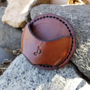 May include: A brown leather case with a musical note design. The case has a flap that folds over to protect the contents.