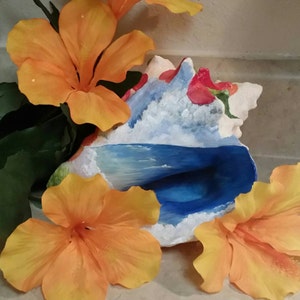 May include: A seashell painted with a blue ocean wave and white clouds. The shell is surrounded by three orange hibiscus flowers.