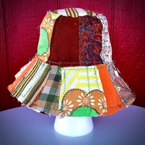 May include: A bucket hat constructed from various fabric patches in diverse colors and patterns, including orange, yellow, brown, green, and floral prints. The pieces are joined with visible zigzag stitching, creating a textured, multi-fabric design.