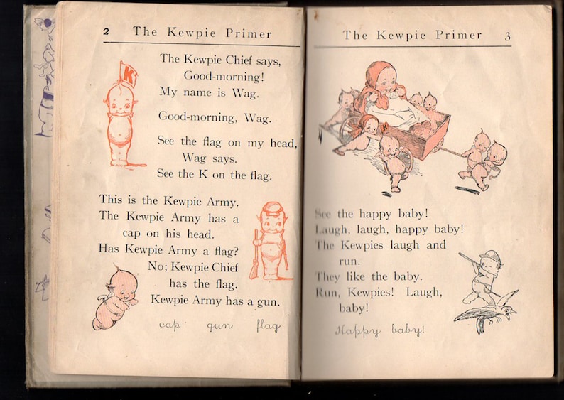 May include: Open book pages from "The Kewpie Primer" featuring illustrations of Kewpie dolls. The left page shows a Kewpie with a flag, text includes "Good-morning!" and "My name is Wag." The right page depicts Kewpies in a wagon.