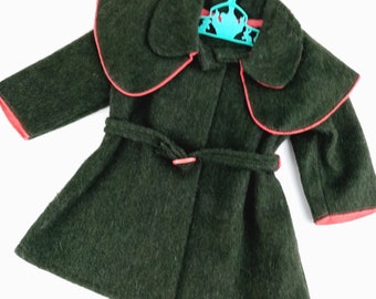 Puede incluir: Un abrigo verde oscuro con cinturón a juego y cuello grande. El abrigo tiene un ribete rojo alrededor del cuello y los puños. Cuelga de una percha turquesa.