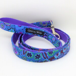 May include: A blue dog leash with a vibrant floral pattern in shades of blue, purple, green, and pink. The leash has a purple handle and backing, with a silver metal clasp. The brand name "CRYSTAL WOLF" is printed on a black label.