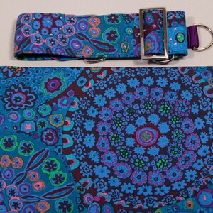May include: A dog collar and matching fabric featuring a vibrant floral pattern in shades of blue, teal, purple, and pink. The collar has a silver-colored buckle and a purple loop for leash attachment.