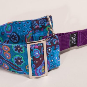 May include: A decorative dog collar with a vibrant floral pattern in shades of teal, purple, and orange. The collar features sparkling embellishments and a purple nylon strap with a metal D-ring and buckle. The brand name "Crystal Wolf" is visible.
