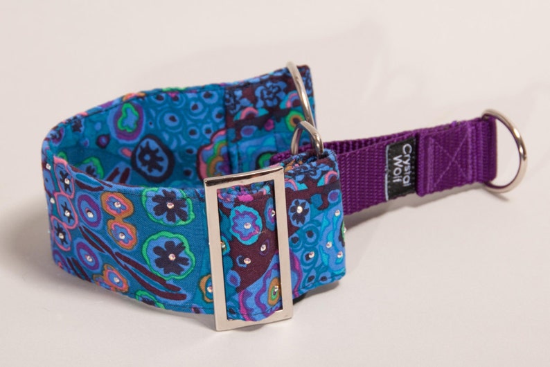 May include: A decorative dog collar with a vibrant floral pattern in shades of teal, purple, and orange. The collar features sparkling embellishments and a purple nylon strap with a metal D-ring and buckle. The brand name "Crystal Wolf" is visible.