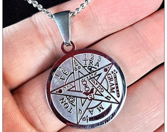 May include: A silver necklace with a round pendant featuring a five-pointed star with the words "1 2 3 TRA", "2 TE", "GRAM", "TON", "MA" and other symbols inscribed around it.