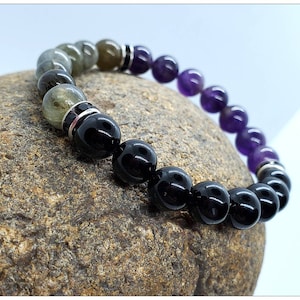 May include: A beaded bracelet with green, black, and purple beads. The bracelet is made of natural stones and is designed in a gradient pattern.