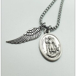 May include: Silver chain necklace with a silver angel wing charm and a silver oval pendant featuring an image of Saint Raphael. The pendant has the text "St. Raphael" and "1917" inscribed on it.