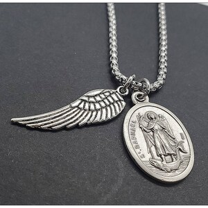 May include: Silver chain necklace with a silver angel wing charm and a silver oval pendant with the inscription "S. Raphael" and an image of an angel.