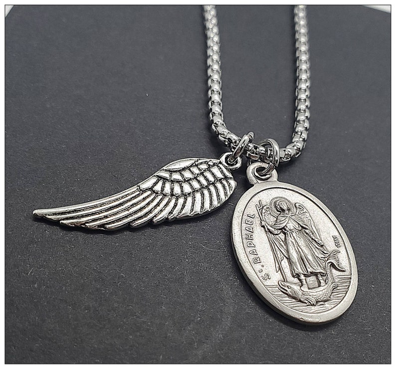 May include: Silver chain necklace with a silver angel wing charm and a silver oval pendant with the inscription "S. Raphael" and an image of an angel.