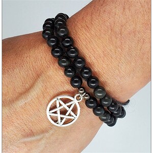 May include: A black beaded bracelet with a silver pentagram charm. The bracelet is made of black obsidian beads and is double-layered.